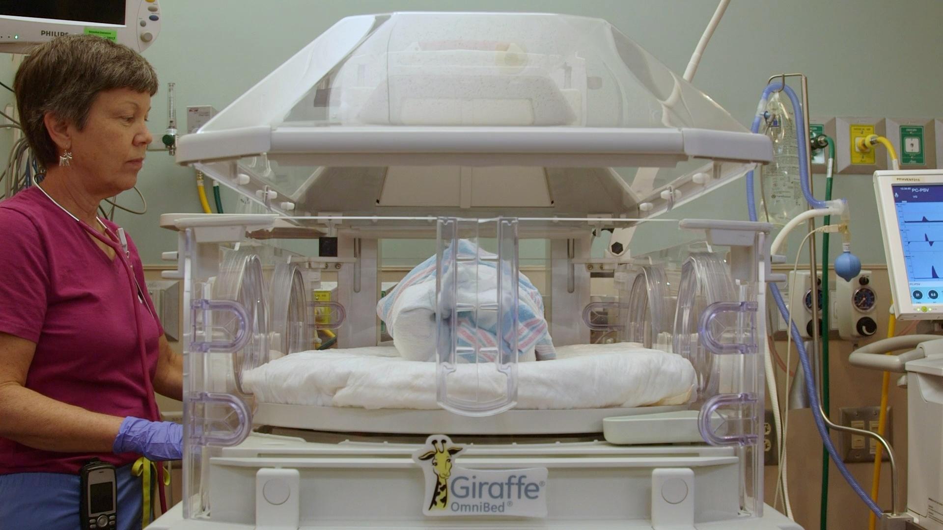A healthcare professional standing next to an incubator in NICU